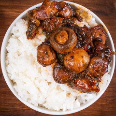 Small bowl with spicy stewed pork with mushrooms in oriental style with spices, hot peppers and boiled rice on a wooden table - top view, close-up