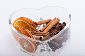 Slices of dried oranges, cinnamon and cardamom in a heart-shaped glass dish