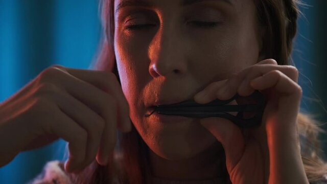 Jaw harp player. Portrait of the young woman in authentic clothes playing jaw harp. Extreme close up portrait of the musician