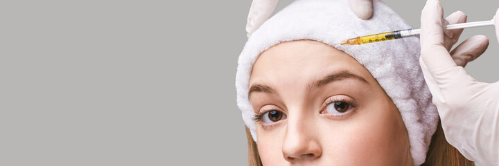 Forehead injection at spa salon. Doctor hands. Pretty female patient. Beauty treatment. Healthy skin procedure. Young woman face. Grey background. Plasmolifting rejuvenation. Dermatology mask