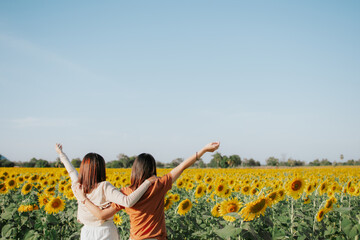 Two women are standing in a field of sunflower and hugging each other. Their hands are raised up to the sky. Friendship concept and copy space.