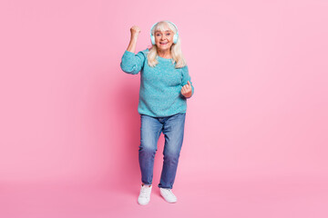 Full length photo of pensioner lady dance raise fist wear blue sweater denim jeans earphones sneakers isolated pink color background