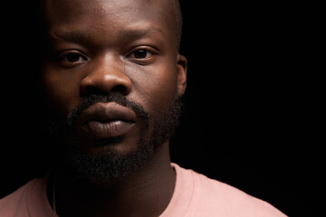 Obraz premium portrait of a dark-skinned handsome guy on dark background in pink sweater stands with serious face and looks in camera