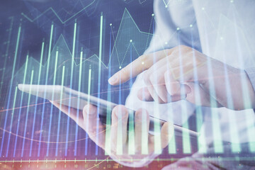 Double exposure of man's hands holding and using a digital device and forex graph drawing. Financial market concept.