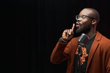 portrait of a dark-skinned handsome guy in brown jacket and black t-shirt stands with a microphone...