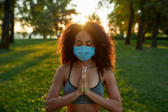 Staying Healthy During Coronavirus Outbreak. Young Mixed Race Woman Wearing Protective Face Mask Meditating And Practicing Yoga Outdoors During Covid 19 Pandemic