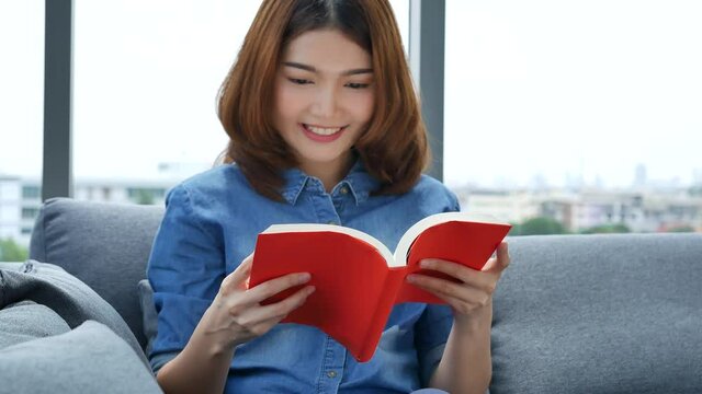 Relax asian woman reading book sitting on sofa in living room holding book to read. Young woman relaxation reader reading open book leisure mind. Happiness beauty woman person smiling face happy time