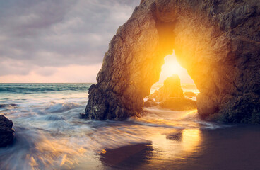 Arched rock formation on beach during sunset
