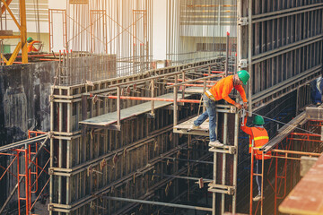 Construction workers in safety uniform install reinforced steel scaffolding at outdoor construction site.