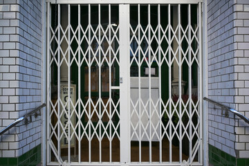 Shuttered security grille in front of a retail store, that had to close during the lockdown due to the coronavirus pandemic crisis with risk of infection with covid-19 - obrazy, fototapety, plakaty