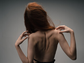 A thin red-haired woman touches herself with her hands behind her back