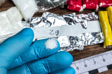 evidence of smuggling traffic: drug powder in the hand of a forensic expert against the background of other arrested materials, cocaine, heroin, spice