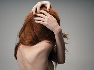 A red-haired woman with bare shoulders touches her head