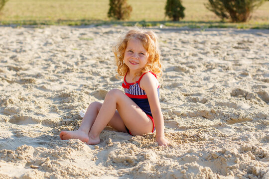 cute little curly-haired girl in a swimsuit sitting on the beach on the sand in summer on vacation