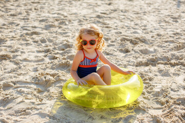 little girl in sunglasses sitting on an inflatable circle on the beach on the sand summer