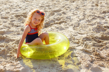 little girl in sunglasses sitting on an inflatable circle on the beach on the sand summer