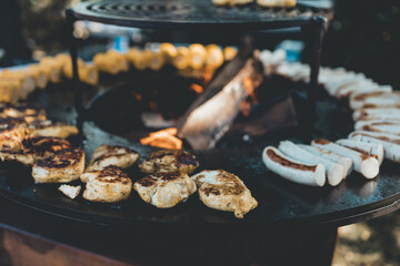 Fleisch und halbe Bratwürstchen auf einem Rundgrill oder Feuerschale