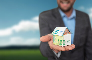 Ein Mann hält ein Haus aus Euro-Banknoten in der Hand