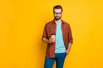 Photo portrait of bearded man in glasses keeping cup with coffee in casual clothes isolated on vivid yellow color background