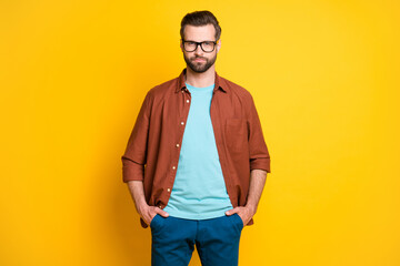Fototapeta premium Photo portrait of clever serious businessman in glasses in casual clothes hands in pockets isolated on bright yellow color background