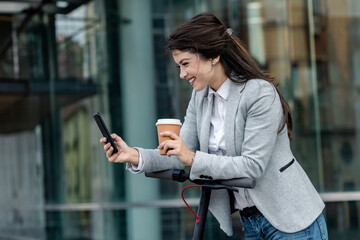 Businesswoman with electric scooter standing in front of modern business building looking at phone.