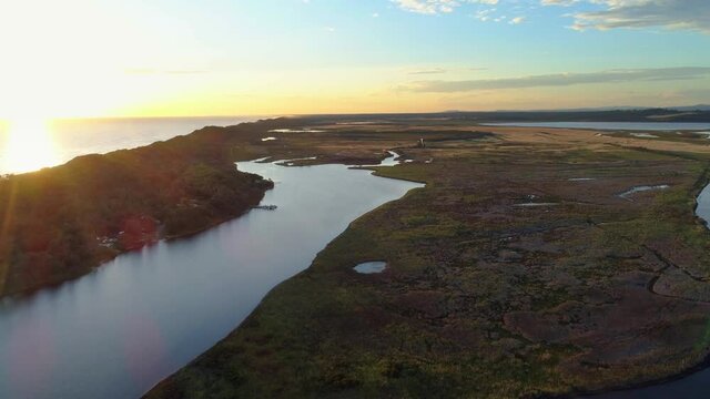 Cinematic flight along ocean coastline and river estuary at sunset in Australia