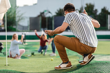 Obraz premium Group of smiling friends enjoying together playing mini golf in the city.