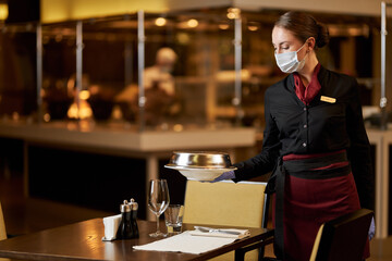 Serious young woman in mask working at restaurant