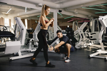 Fototapeta na wymiar A man trains a girl in a modern sports hall. The coach controls the athlete during the exercise. The girl does exercises on the lower part of the body. Fitness in the gym