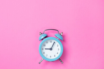 Blue alarm clock on pink background with copy space