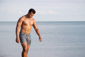Fototapeta na wymiar Muscular model young man walking on sea shore. asia man feeling relax on beach summer vacation