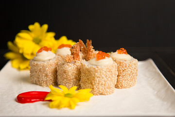 Side view of sushi roll Ebi Tempura with shrimp served with red caviar on top. Yellow camomile flower blossoms, painting brush stroke decorations on square white plate on Black background. Food art
