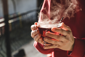 Woman holding hot tea with both hands in cold weather. A cup of tea is steaming.