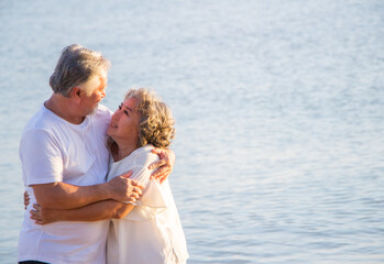 A retired couple embracing each other at the beach with sea background.