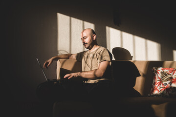 Mustache bald man working with computer in front of the window at sunset.