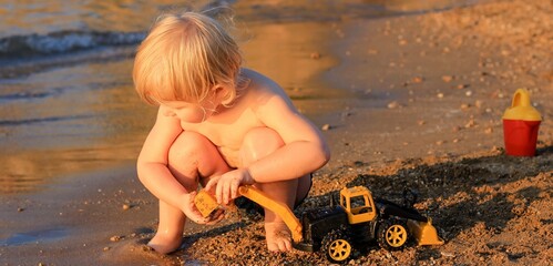 Little boy playing on the beach with a toy car. Summertime, vacation, travel, childhood banner.	
