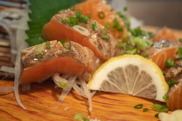 Salmon sashimi burn served with sliced lemon on wood plate.