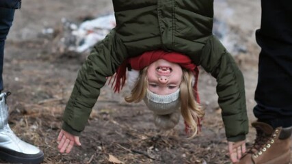 young parents hold their happy daughter by her legs upside down. A little girl hangs upside down in her parents' arms. Family walk in the park.