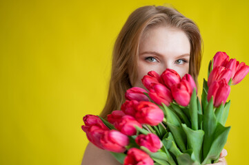 Fototapeta premium Woman with a bouquet of red tulips on a yellow background. Happy girl in a black dress holds an armful of flowers . Gift for Valentine's Day. The most romantic day of the year.