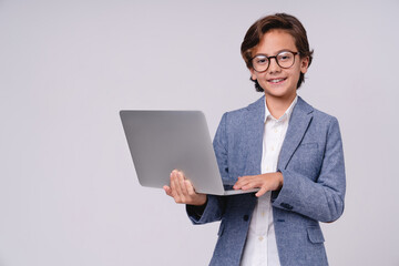 Smart little boy with laptop in formal clothes isolated over grey background