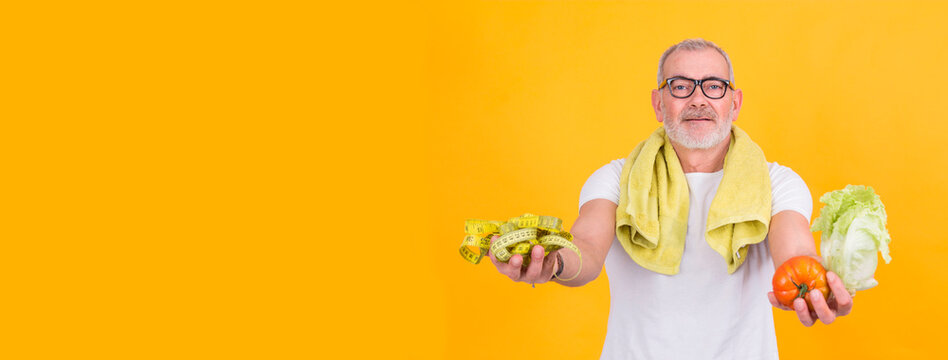 attractive mature man with tape measure in one hand and lettuce and tomato in the other, diet and health concept