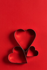 Saint Valentine day minimalistic greeting card, heart-shaped cookie cutters on red background with beautiful shadows
