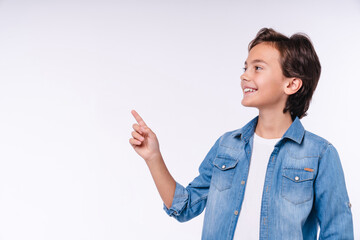 Smart little 10s boy in casual attire pointing at copy space isolated over white background © InsideCreativeHouse