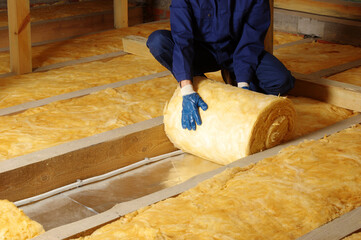 Worker thermally insulating house attic with glass wool