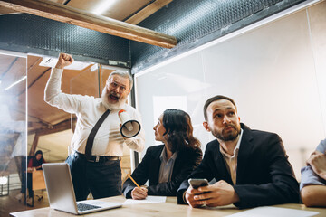 Shouting. Angry boss with megaphone screaming at employees in office, scared and annoyed colleagues listening at the table stressed out. Funny meeting, business, office concept. Screaming mad.