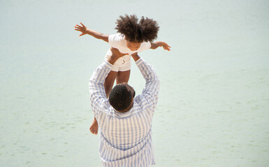Father holding his daughter up high against sky. african american dady hug girl with sea background
