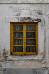 Fototapeta na wymiar Detail of old traditional house in a Portuguese village with yellow wooden window and embroidered curtains. Modest house with dirty damaged white walls and rustic window frame