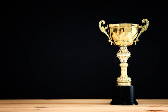 image of gold trophy over wooden table and dark background