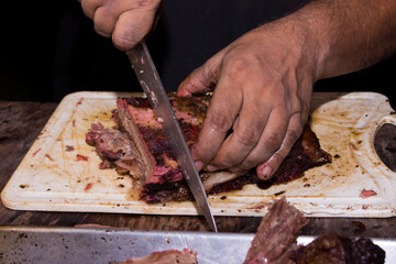 Smoked beef rib being cut with a knife. Rustic food made on the grill and smoked at Pit Smoker. Cutting meat.