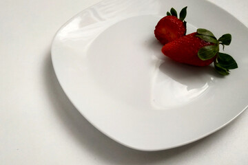 Two strawberries on a plate, one strawberry bitten, close-up, berry on a white glossy plate, place for an inscription.